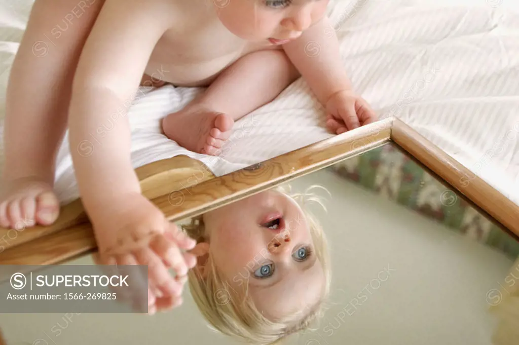 18 month old girl sitting leaning over a mirror