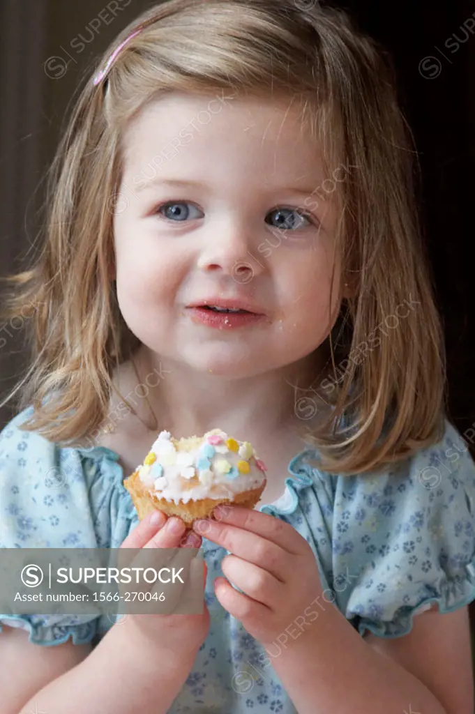 Little girl´s third birthday party, eating a bun, smiling