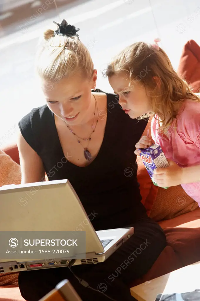 21 year old girl working on a laptop on her knee, with a 3 year old girl watching