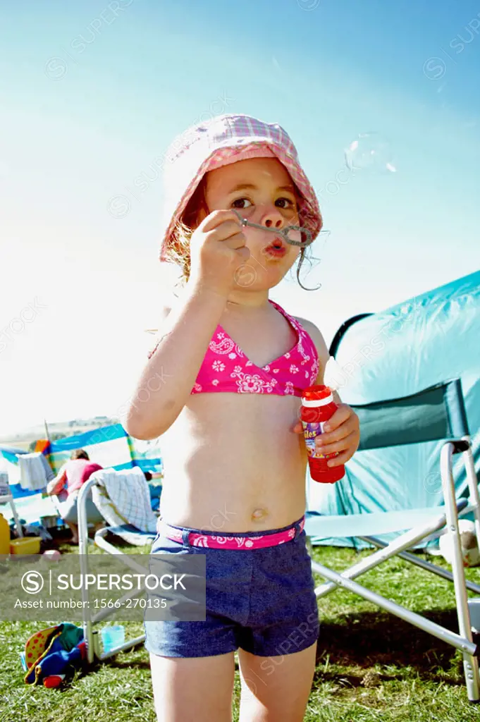 3 year old girl outside in the sunshine,on a camping trip, blowing bubbles