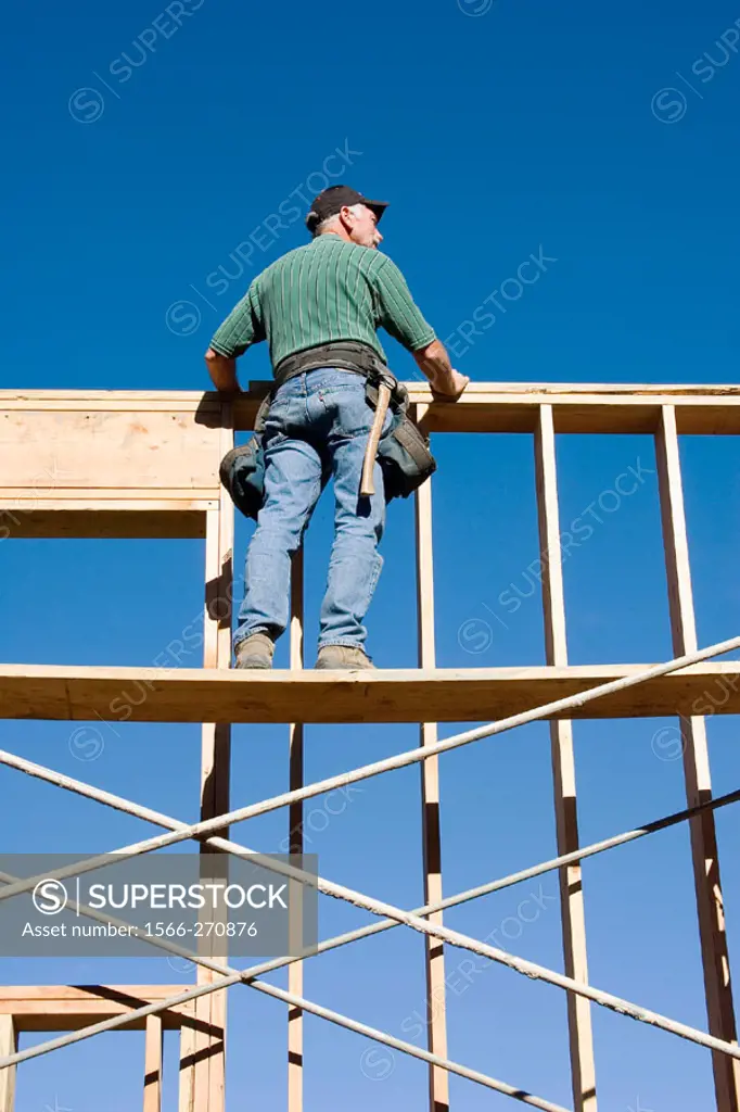 Carpenter standing on scaffolding looking over the top of second story wall at a construction site.