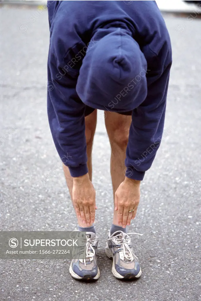 Male jogger stretching by touching his toes.