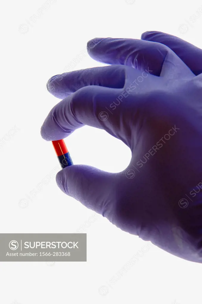 Latex gloved hand holding capsule.