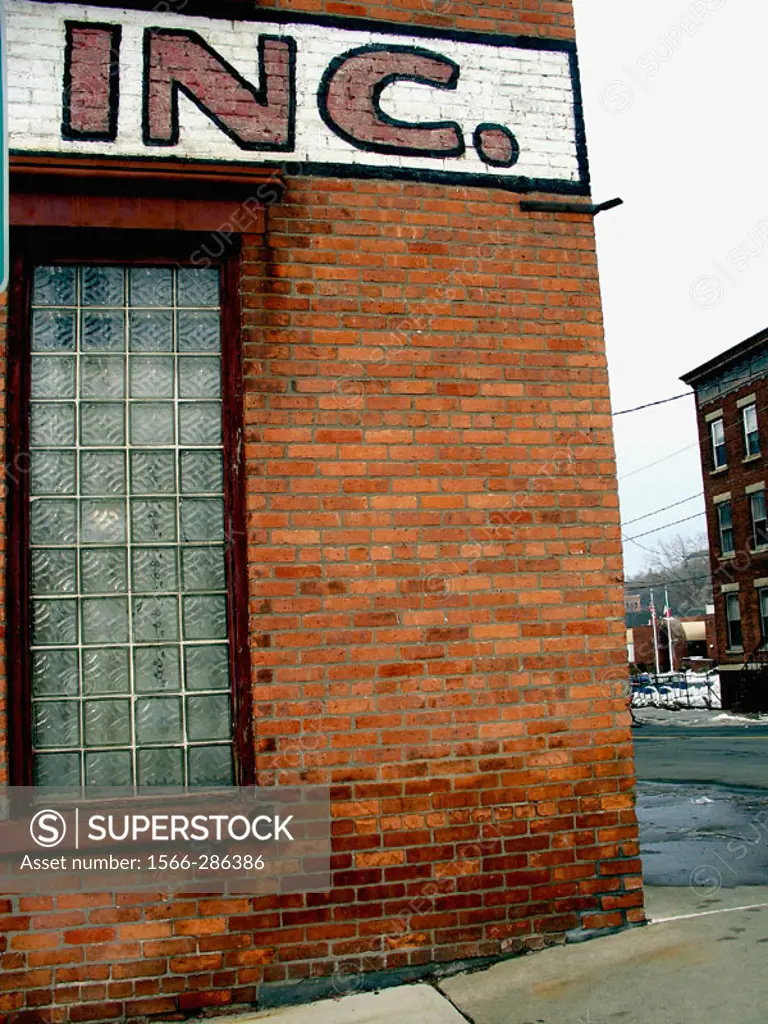 The corner of a brick factory building in New England is captured during winter with the abbreviation INC. featured prominently in the photo.