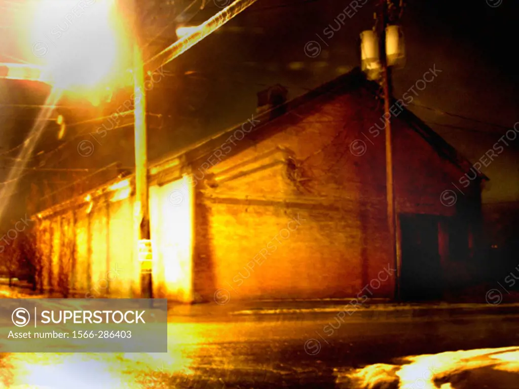 A warehouse on a desolute street corner is captured at night with a slight blur creating a mysterious, painterly effect.