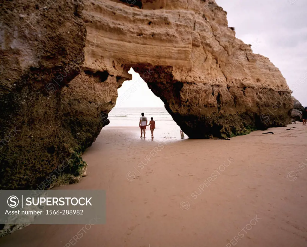 A couple strolls under arch on beach in Algarve