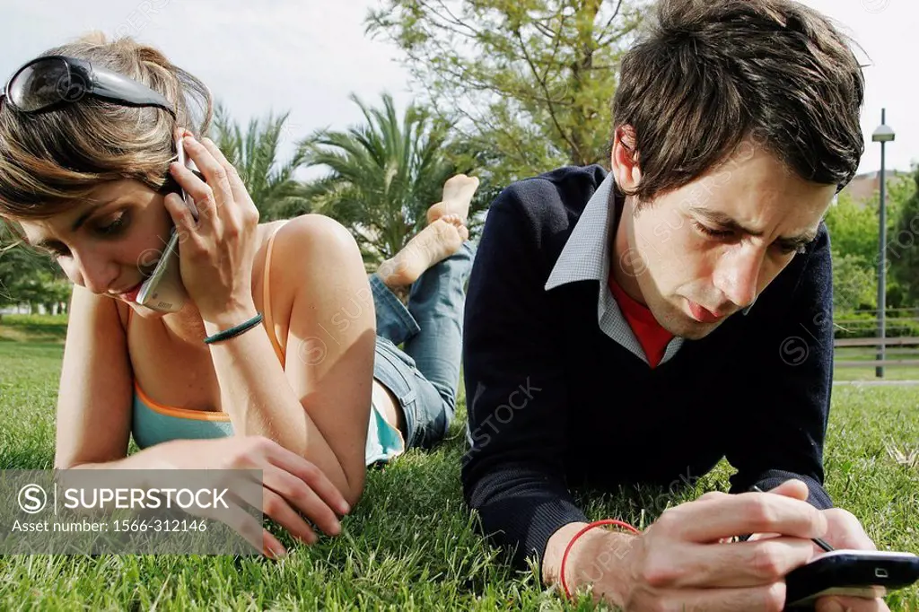 Two people on grass using palm pilot and cell phone