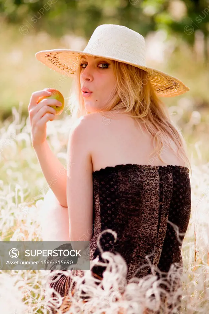 Young blonde woman with apple sitting in green grass