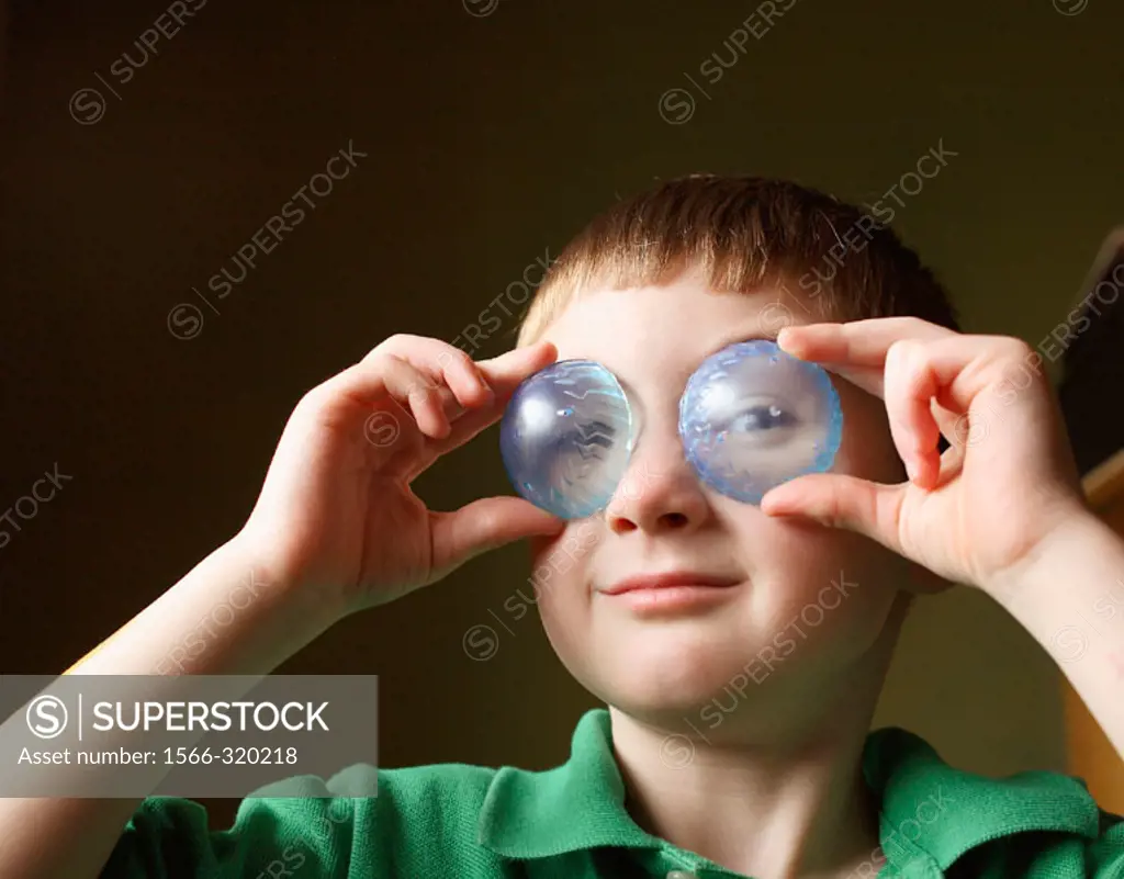 Boy, age five, holding clear blue plastic pieces to his eyes .