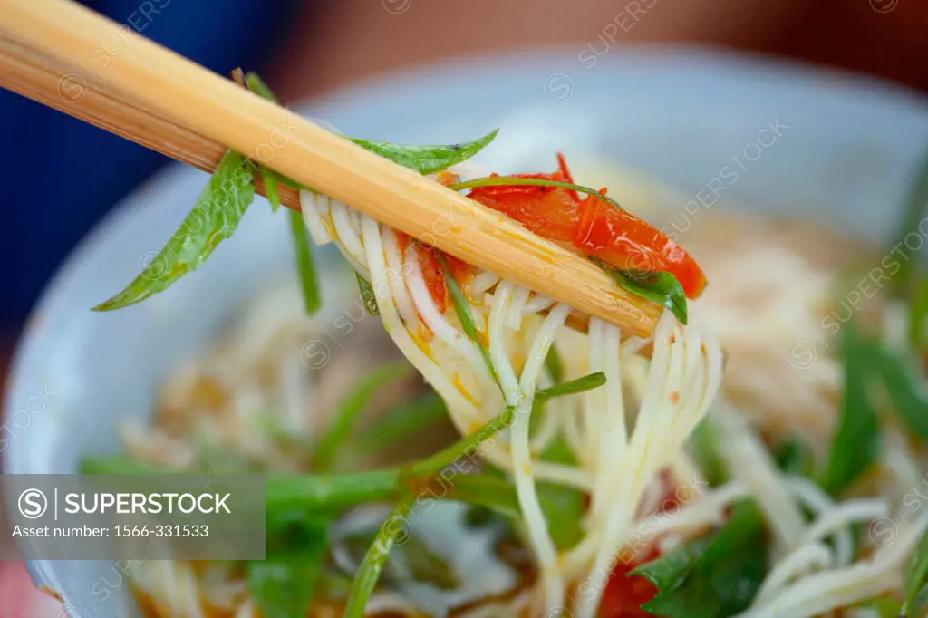 Eating noodle soup as a local speciality with chop sticks on the fresh food market of Hoi An, Vietnam, Southeast Asia