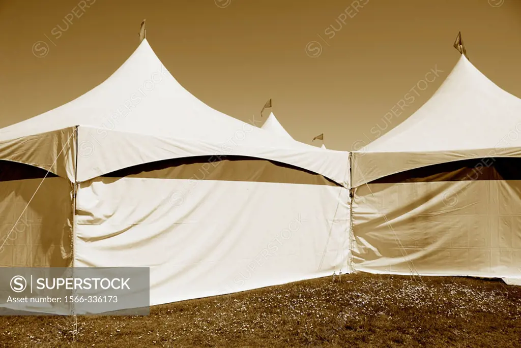 Circus tents with flags flying on top of tents, sepia toned, on grass