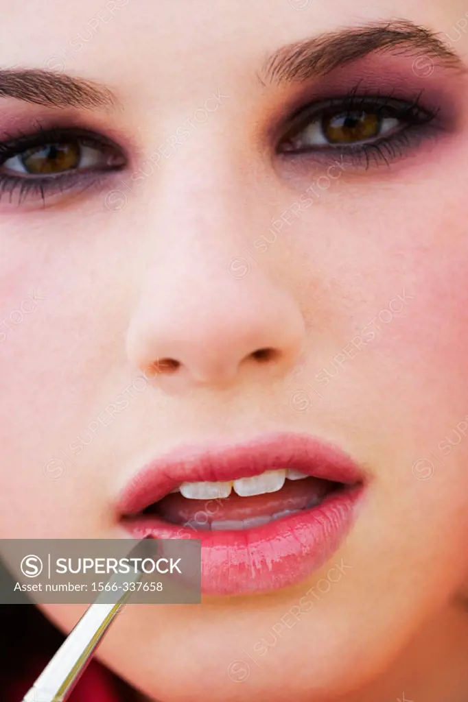 Teen age girl putting makeup on lips.