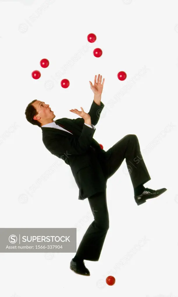Business man struggling unsuccessfully to juggle multiple red balls; one already on ground.