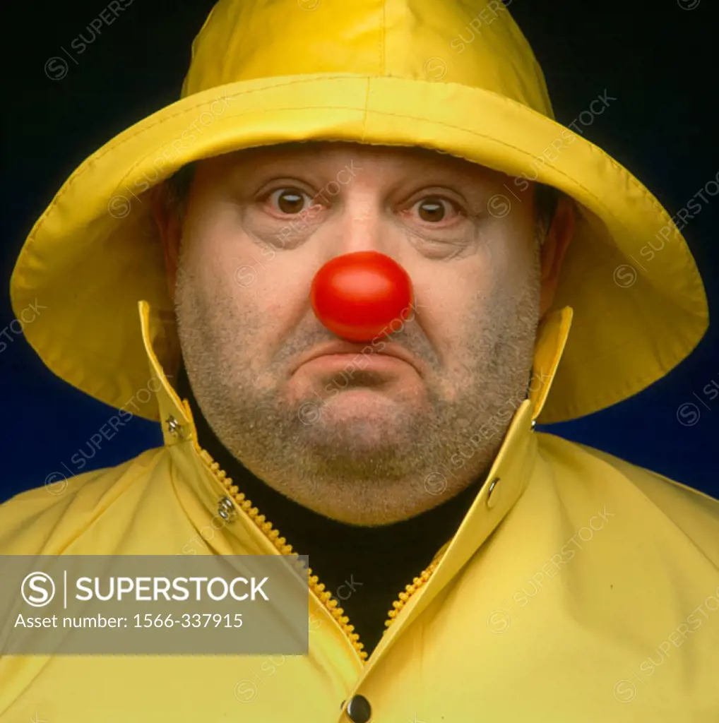 Overweight man in yellow raingear with red clown nose; looking sad.