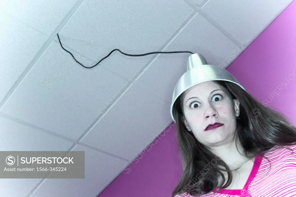 Young woman with a metal hood, which is attached to a wire dropping down from the ceiling, setting on her head.
