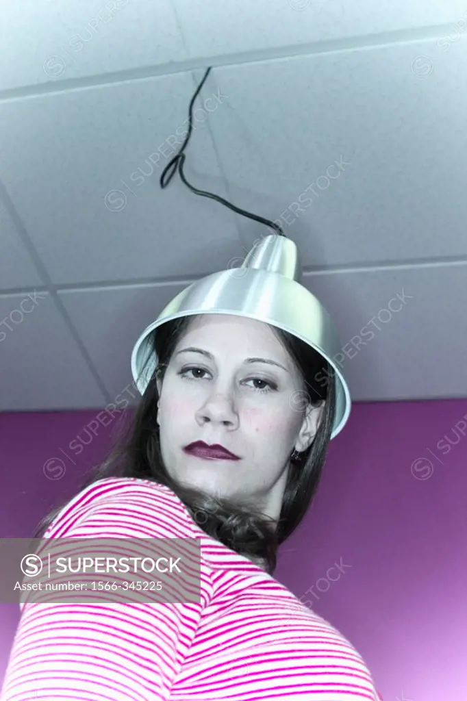 Young woman with a metal hood, which is attached to a wire dropping down from the ceiling, setting on her head.