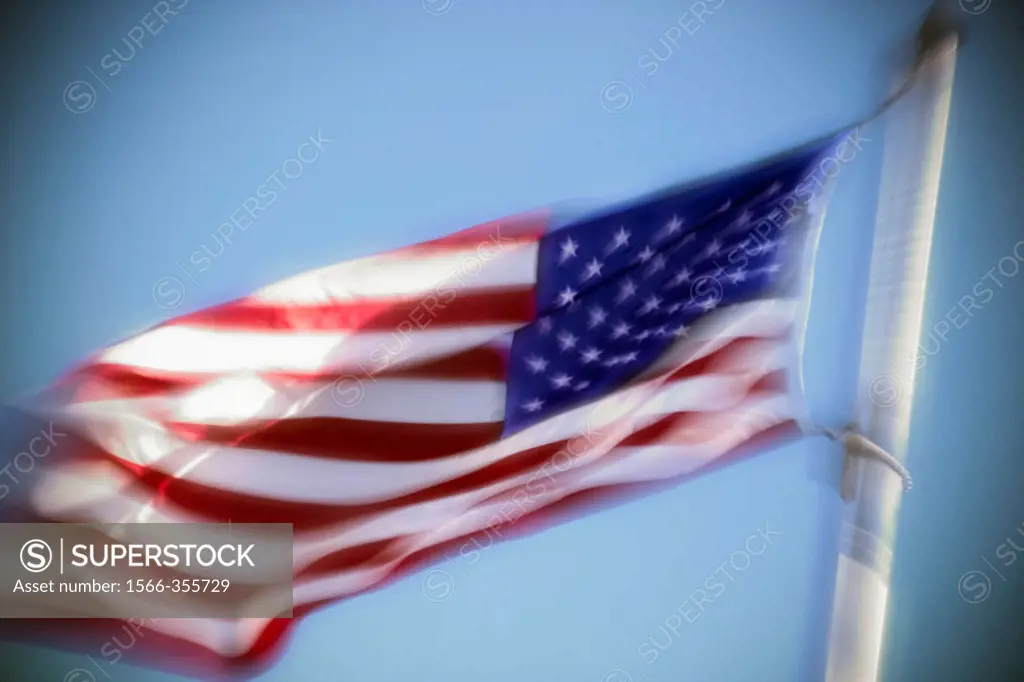 An American flag billowing in the wind against a blue sky.