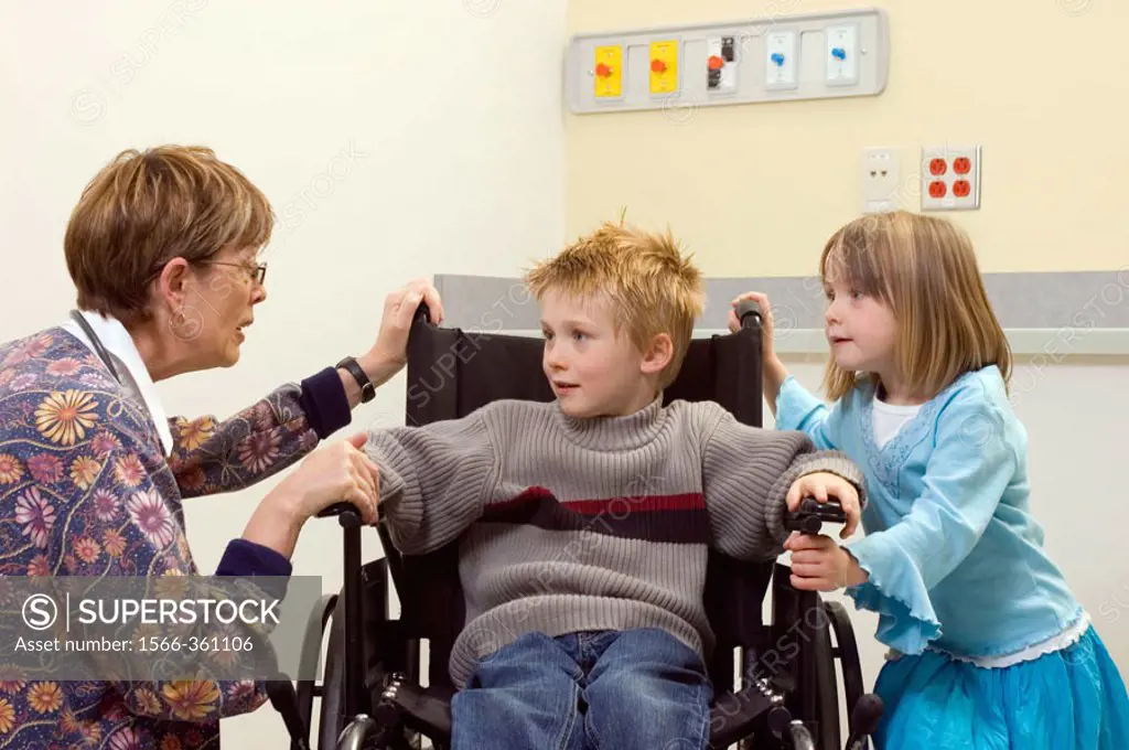 5 year old girl and 7 year old boy in a hospital room with a nurse, the boy is in a wheelchair.