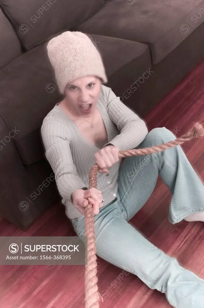 Young woman, wearing a hat and sitting on the floor, pulling on a rope.