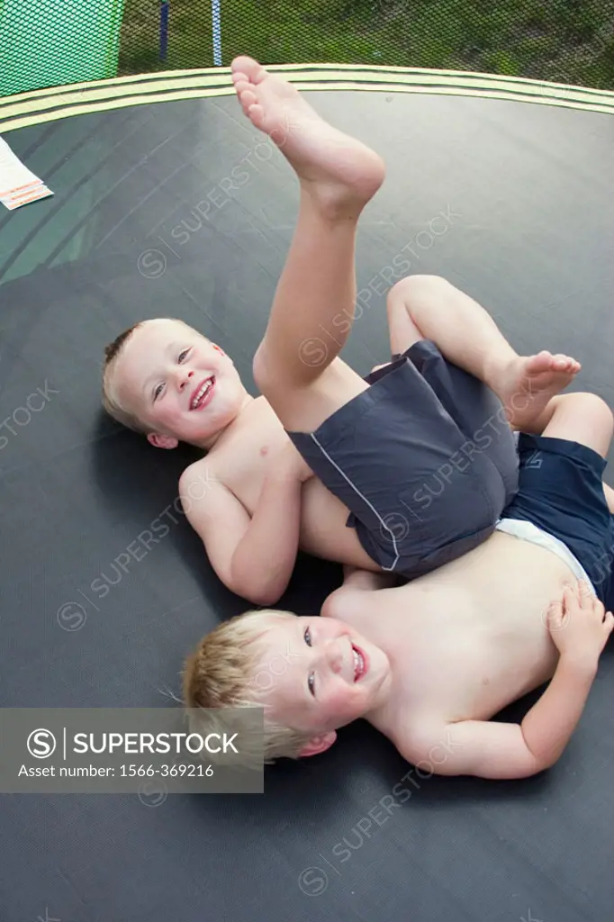3 and 5 year old boys lying on their backs on a trampoline, laughing into camera