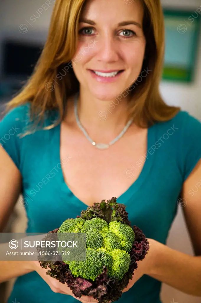 Caucasian mother holding bouquet of vegetables including broccolli.