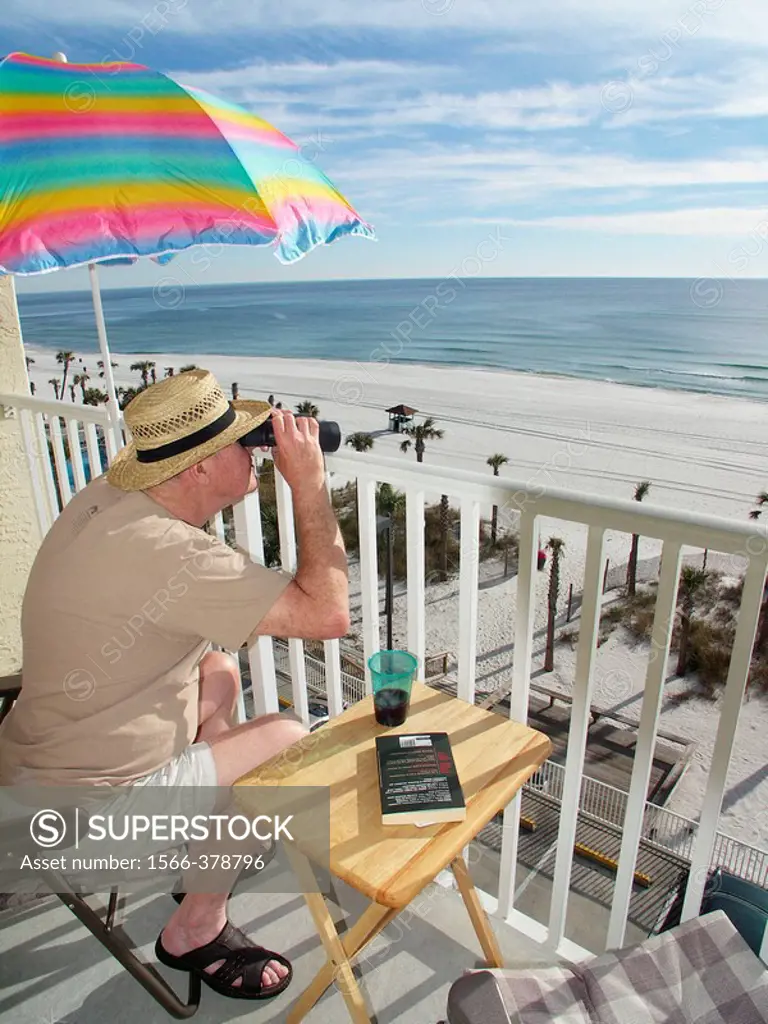 Elderly man looking through binoculars from his balcony