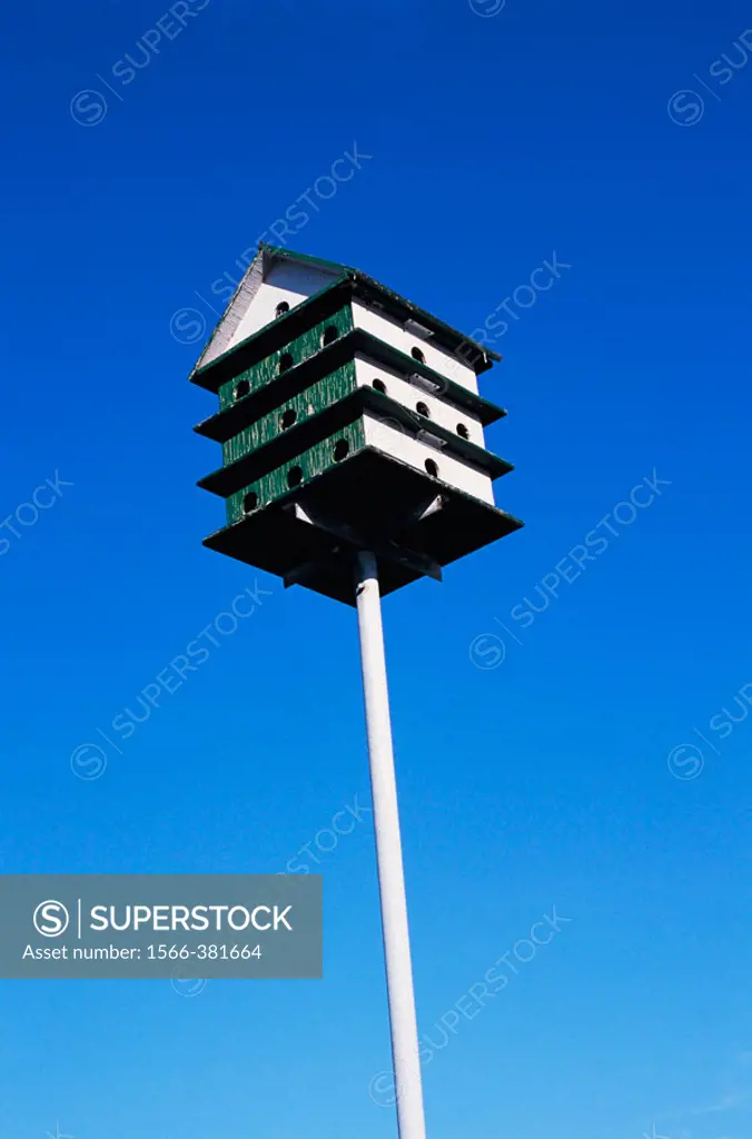 Green and white wooden multi-stored birdhouse on a metal pole