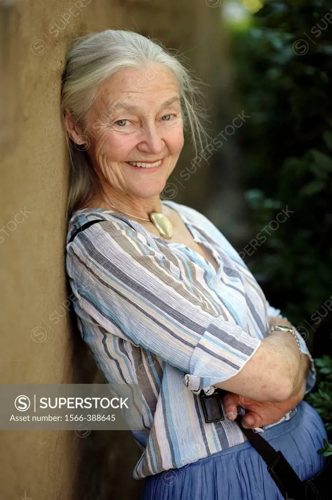 Senior woman leaning on wall and smiling in the camera