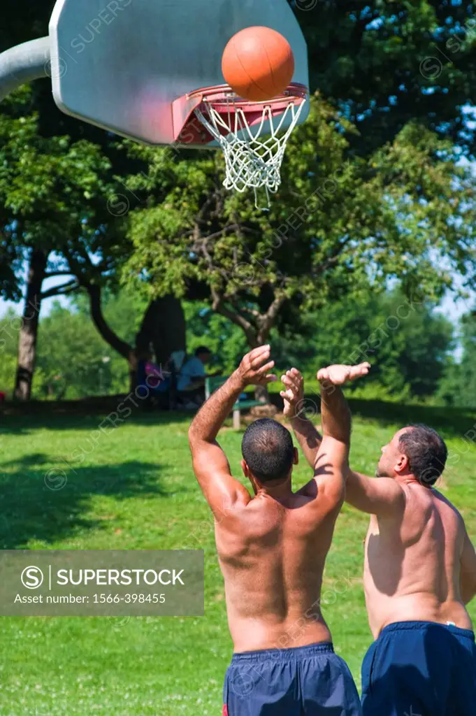 Two middle-age Spanish men playing basketball at a local park.