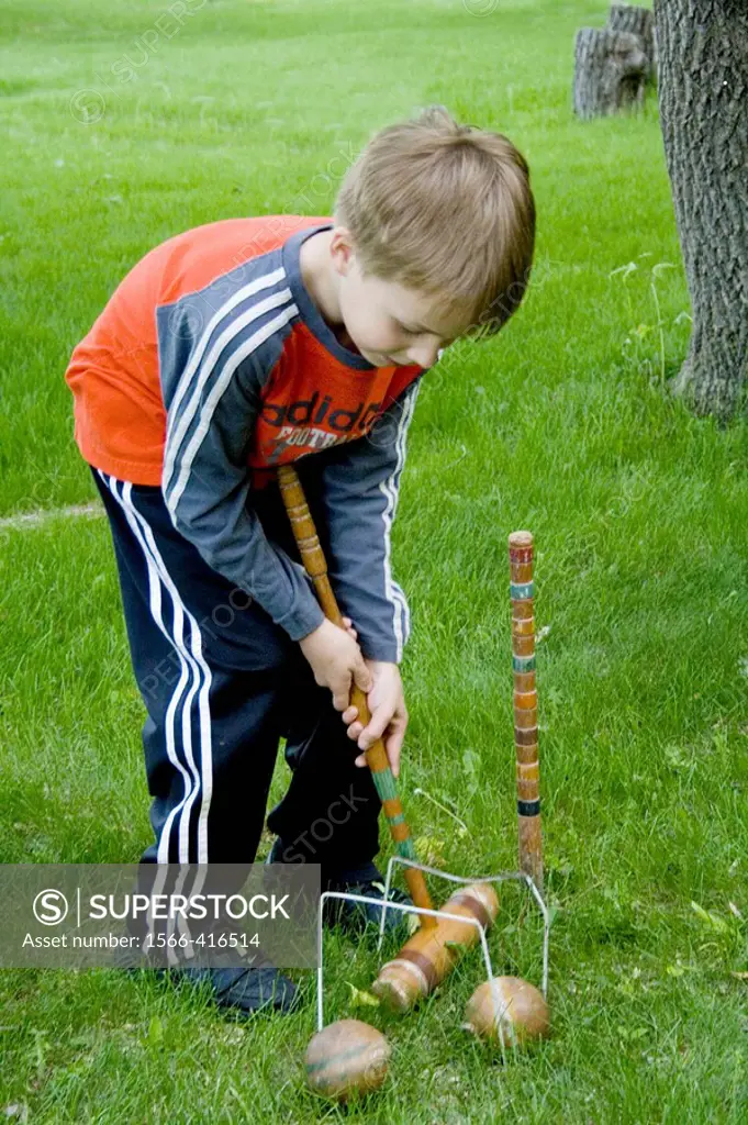 Boy age 7 returning wooden ball through double croquet wickets with a long-handled mallet  Clitherall Minnesota USA