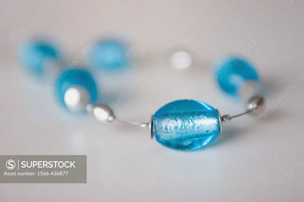 A necklace consisting of large blue glass beads on a silver wire. One bead is in focus in the foreground and the rest fall out of focus on the light g...