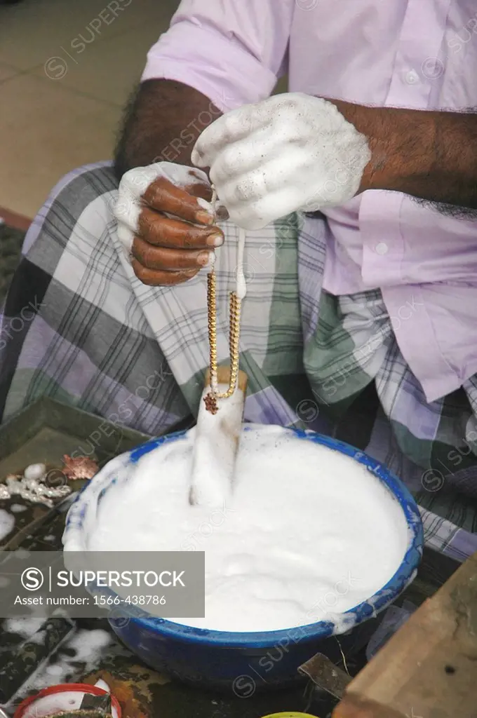 Kandy Sri Lanka: a goldsmith washing a gold necklace in the street