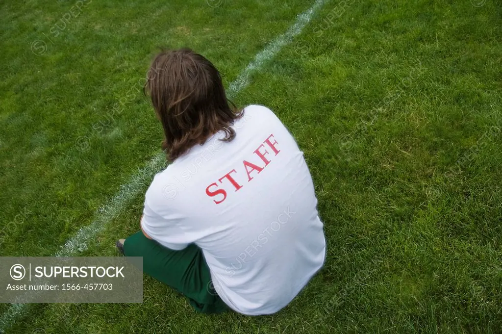 Young man, with ´Staff´ written on the back of his shirt, at a park.