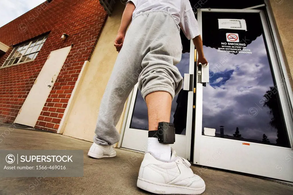 Wearing an electronic ankle monitor, a teenage offender enters a county parole facility in Santa Ana, CA. An ankle monitor is a device that individual...