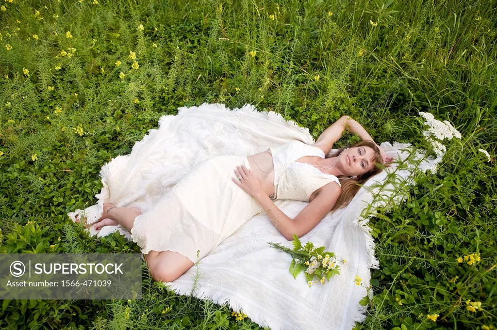 Woman in white dress lying down in meadow with wildflowers