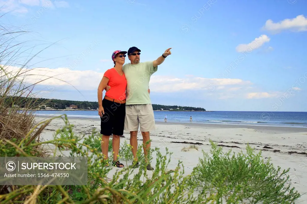 a couple walking on the beach and pointing at something