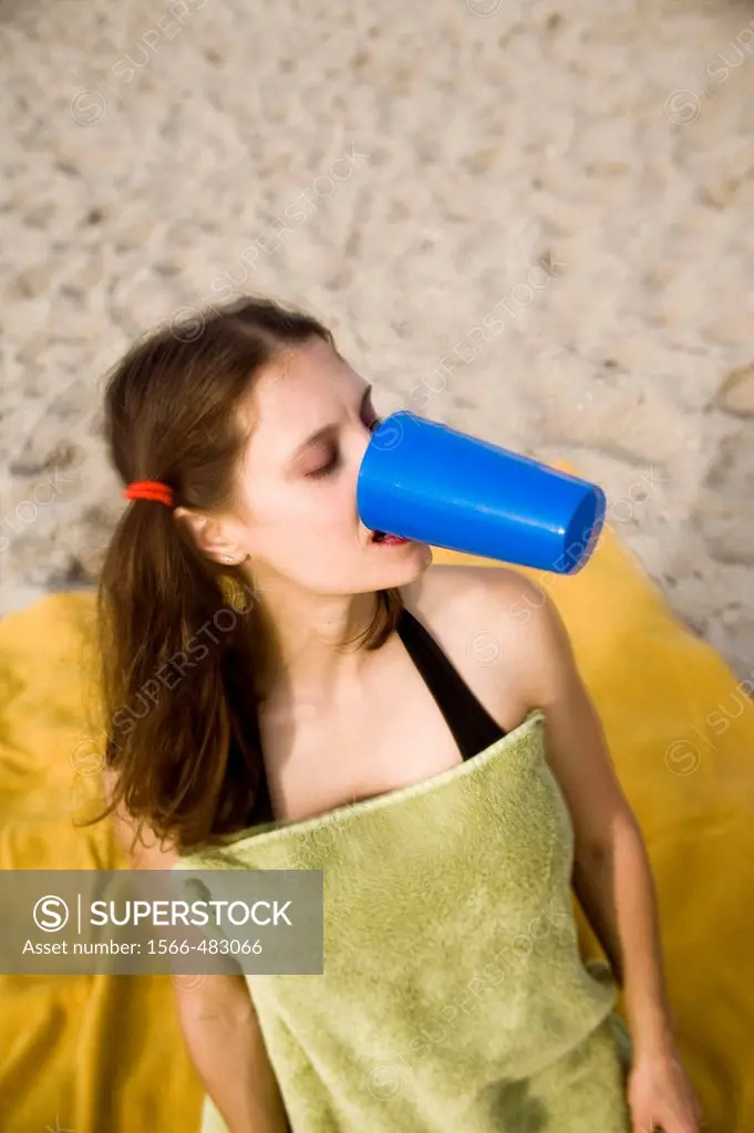 Young woman, at the beach, holding a plastic cup in her mouth.