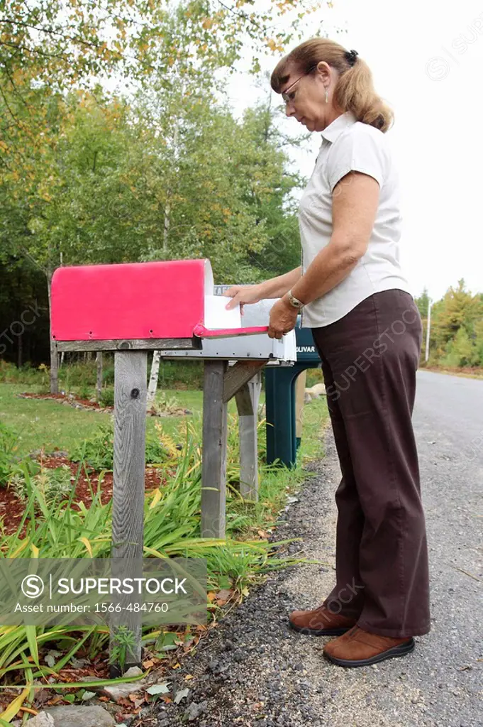 a woman retrieving mail from a rural mailbox -a public box in which mail is placed for pickup and delivery by the post office.