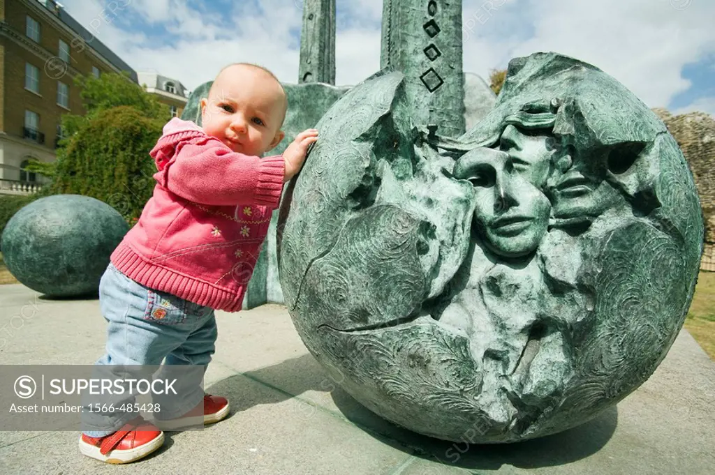 Baby girl pushing a ball of the contemporary sculpture near Reading Abbey Berkshire, England