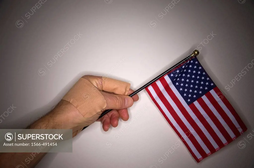 Close_up of a man´s bandaged hand holding a small American flag.