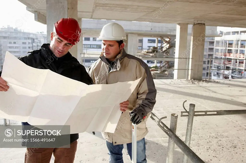 Architect and construction worker looking at blueprints, personal protective equipment, housing construction, concrete skeleton