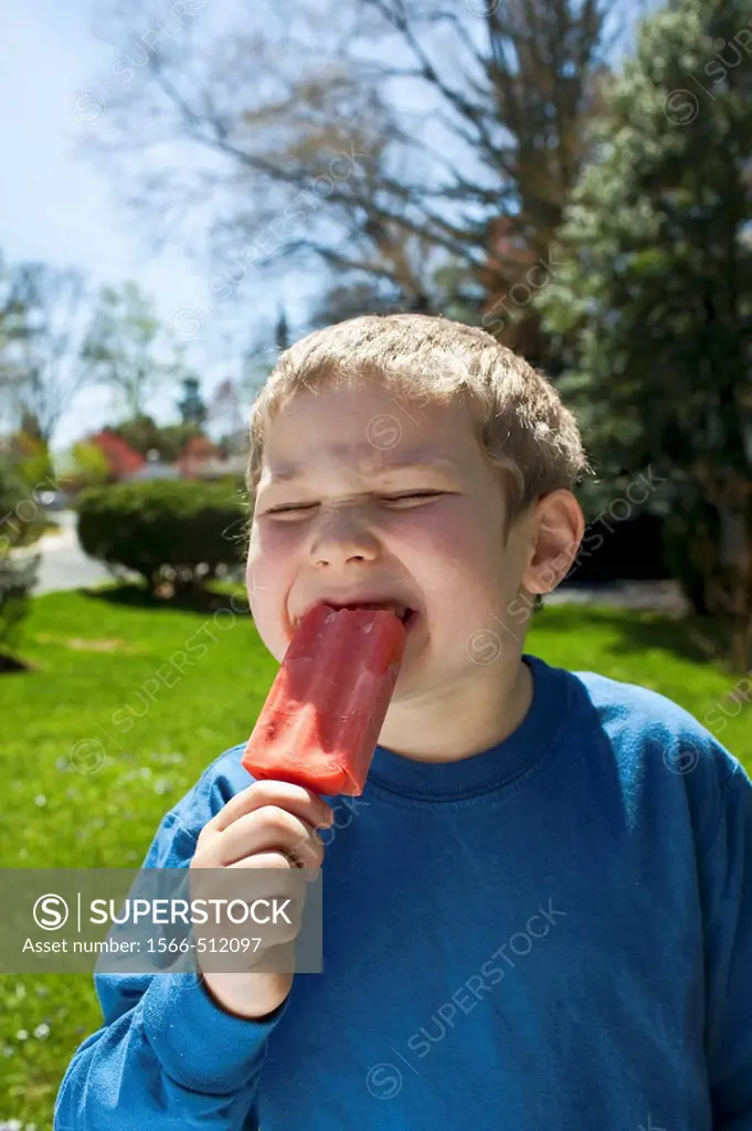 Boy enjoying a red ice pop or popsicle.