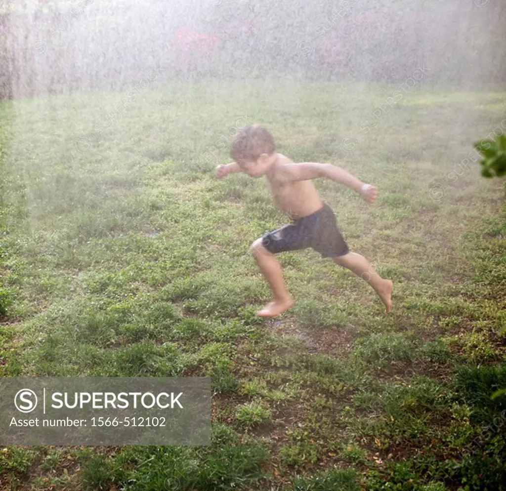 Boy running through a sprinkler outside in his backyard on a warm day.