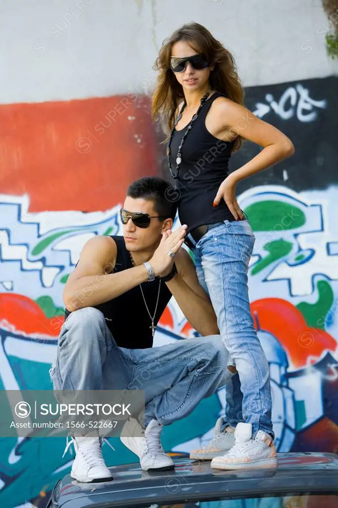 Young couple is standing on a car roof in front of a colorful street wall