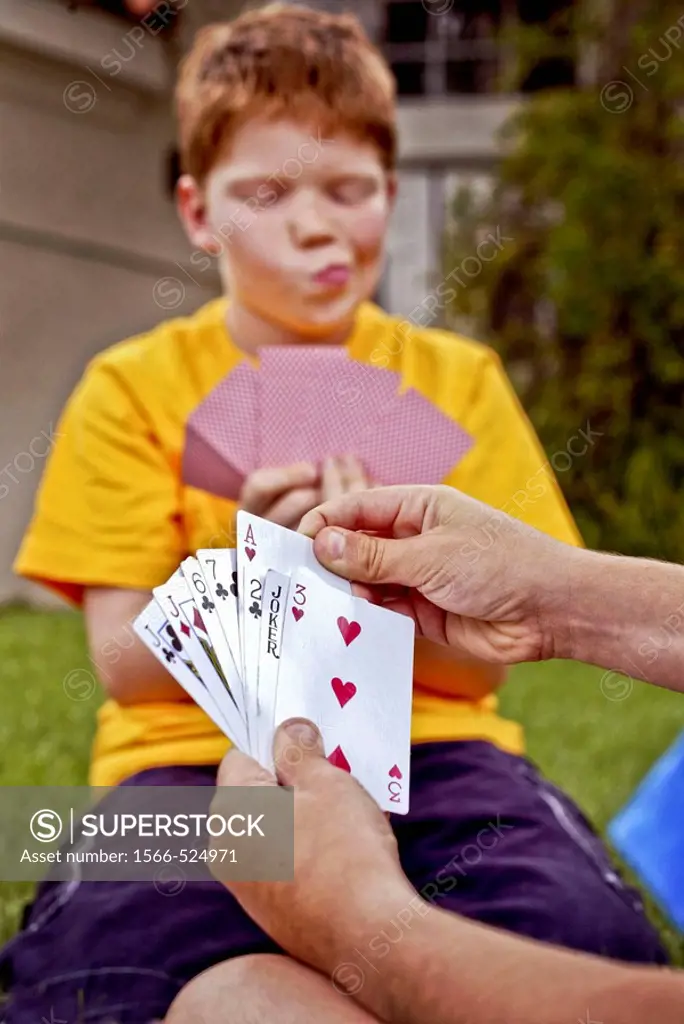 A ten-year-old Caucasian red-headed boy evaluates his hand as he plays cards outdoors in Laguna Niguel, CA  Note partner´s cards in foreground