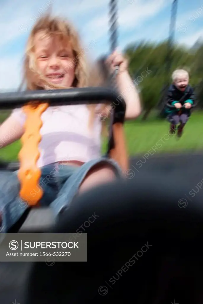 5 year girl and 2 year boy playing on swings, happy expressions, motion blurred