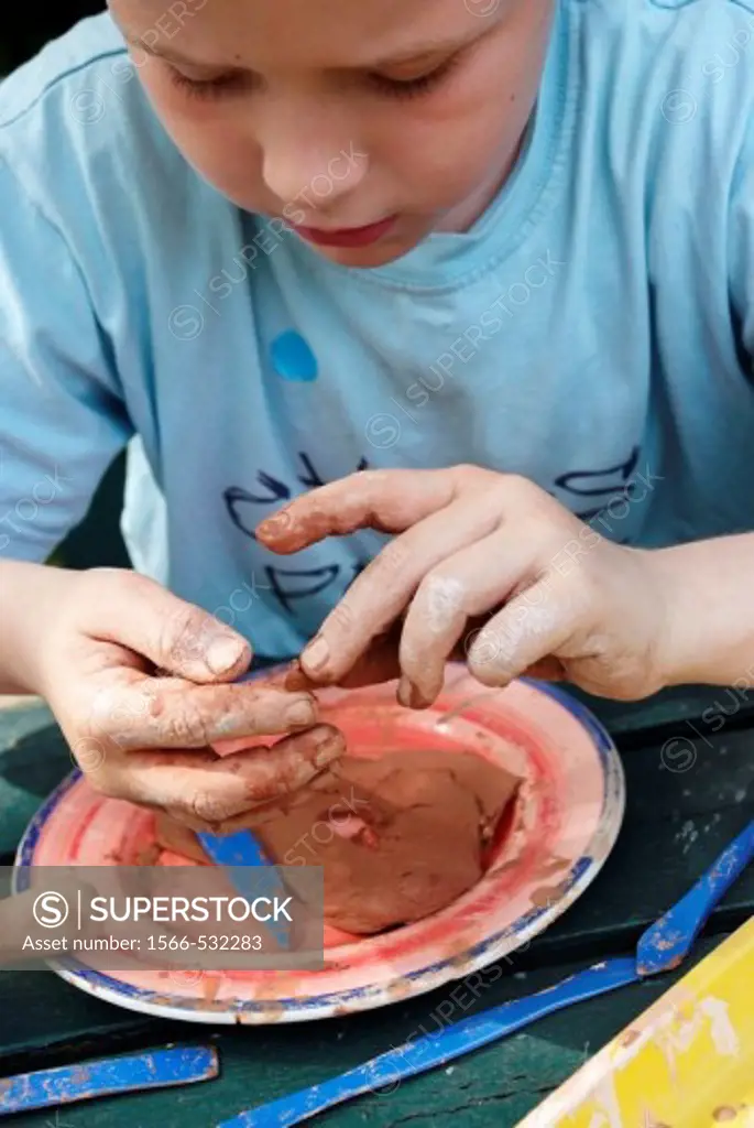 Head and shoulders 6 year boy sitting at table making clay objects