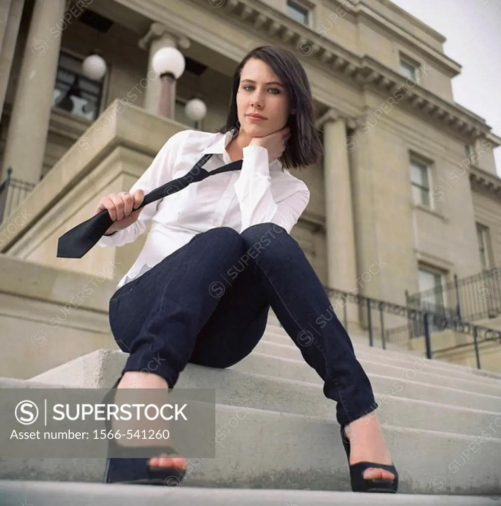 Woman sitting on steps of Public Building pulling on her necktie.