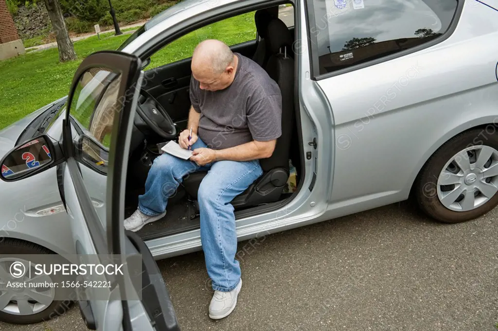 Man sitting in his car, filling out a form