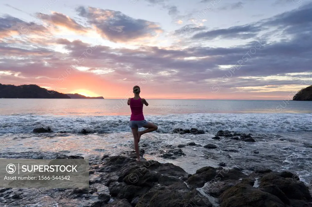 Young woman doing yoga at sunset in front of ocean surf at Playas del Coco, Costa Rica